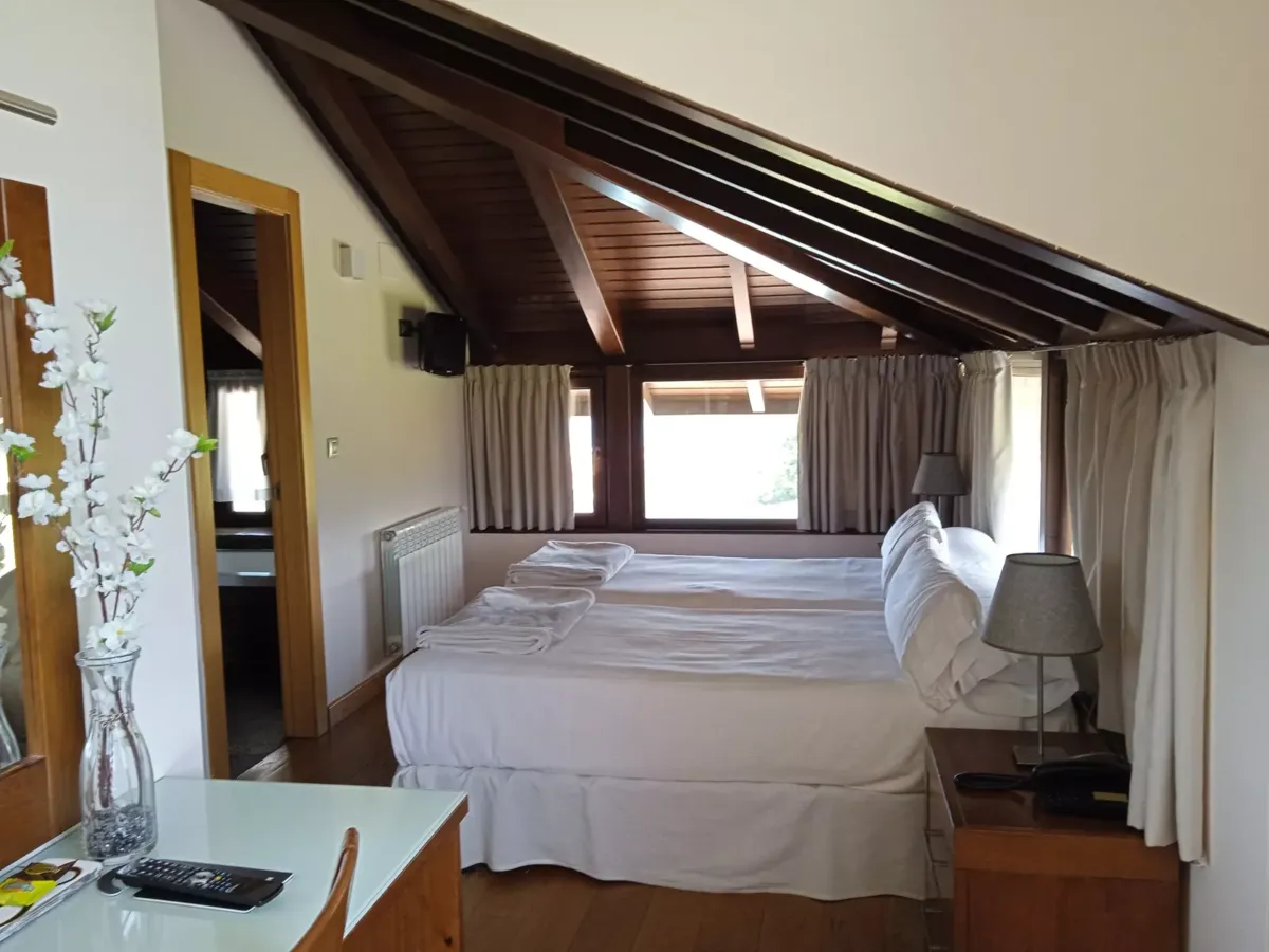 Habitación con dos camas, mesillas y escritorio abuhardillada